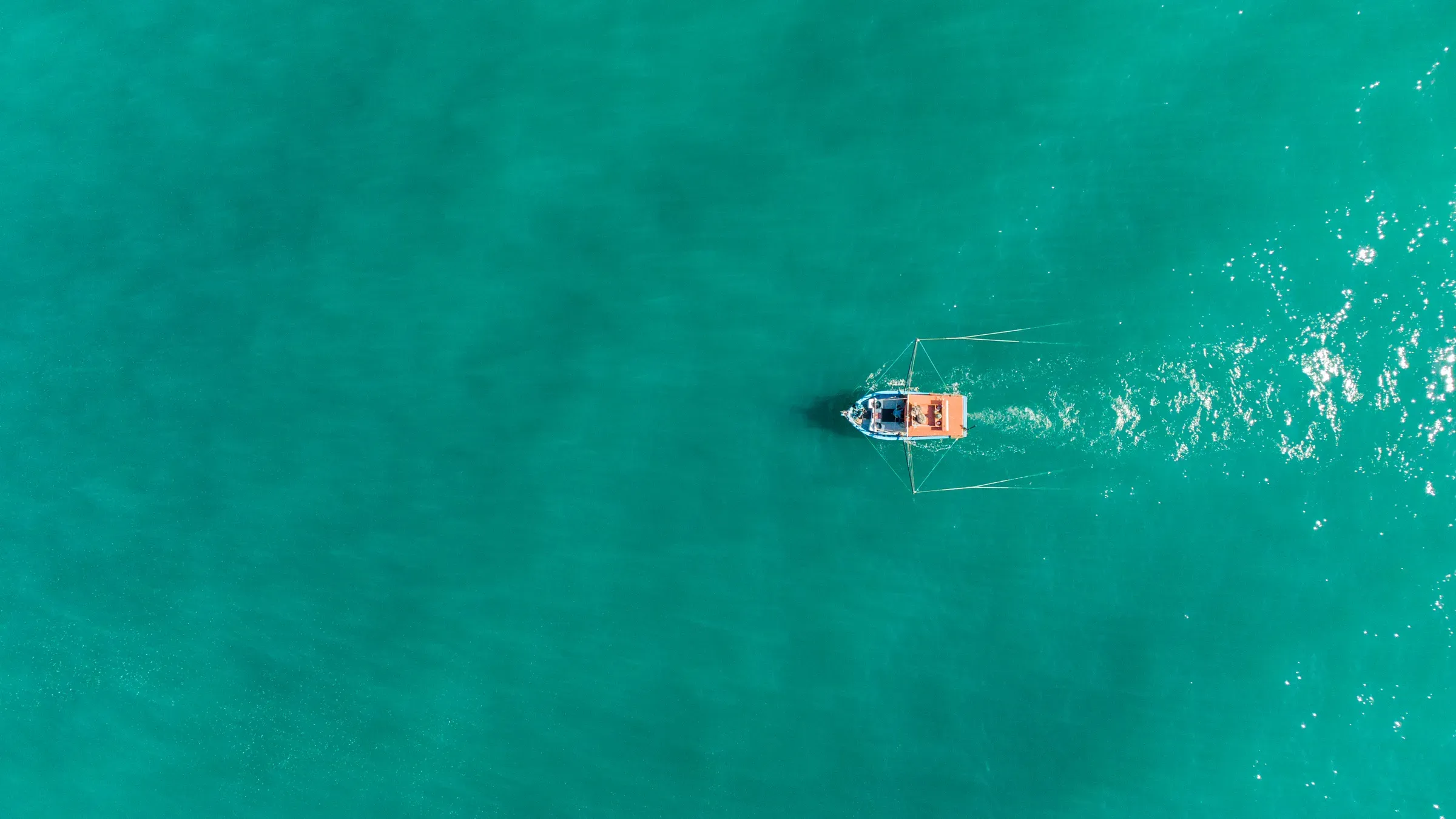 Um barco navega no mar verde-azulado de Ubatuba, visto de cima, deixando um rastro de espuma