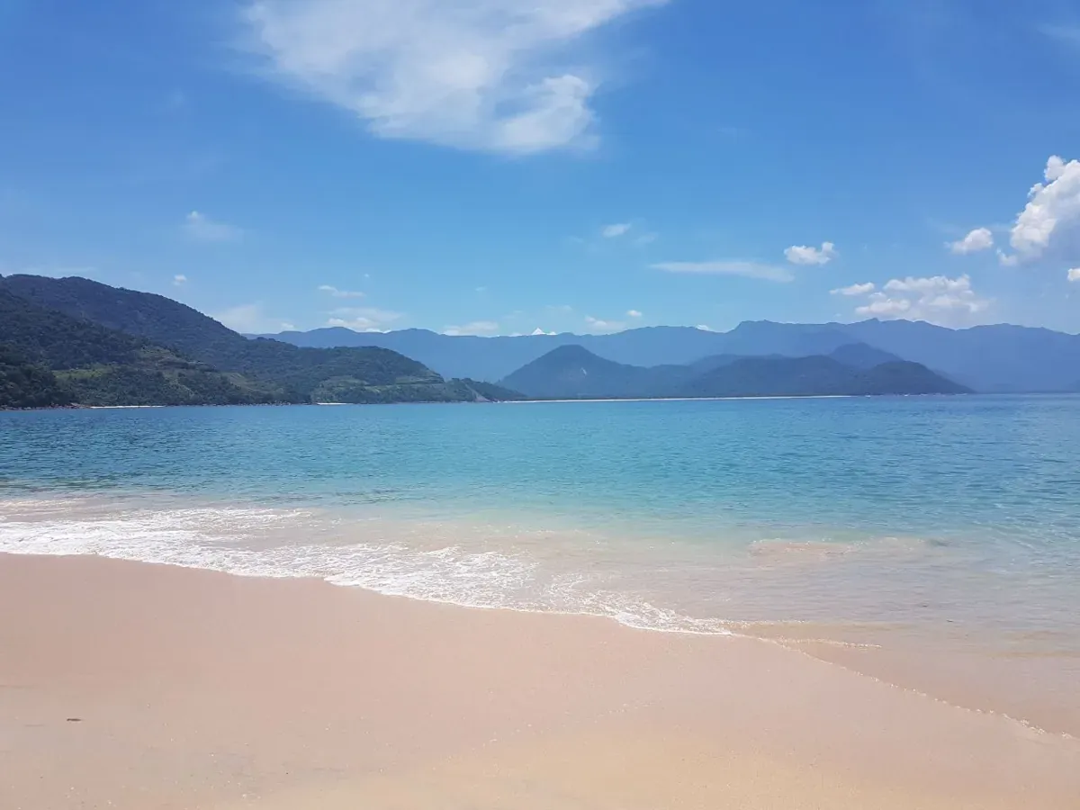 Areia clara e mar azul-turquesa na Ilha do Prumirim, com a serra ao fundo